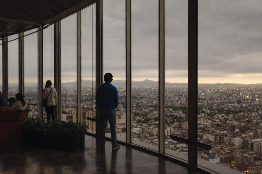 Wide view over central Mexico City rooftops and distant volcanoes seen from a high open-air observation deck